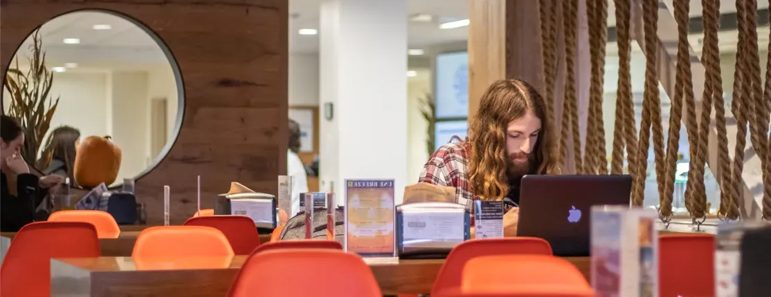 A student works on their laptop in the Commons dining room